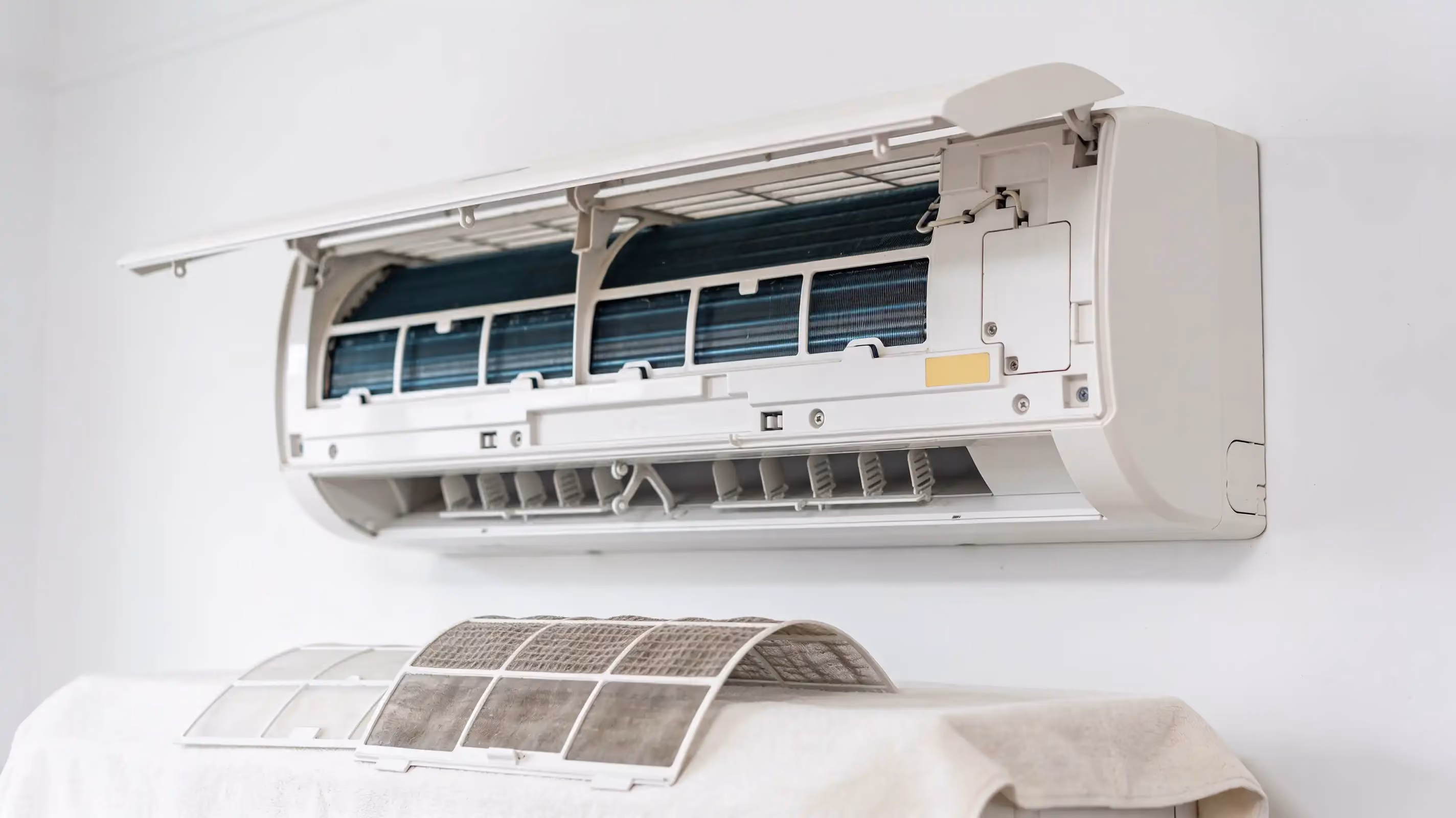 A wall split system with its front panel lifted open and its two dusty mesh filters out, resting on a white cloth