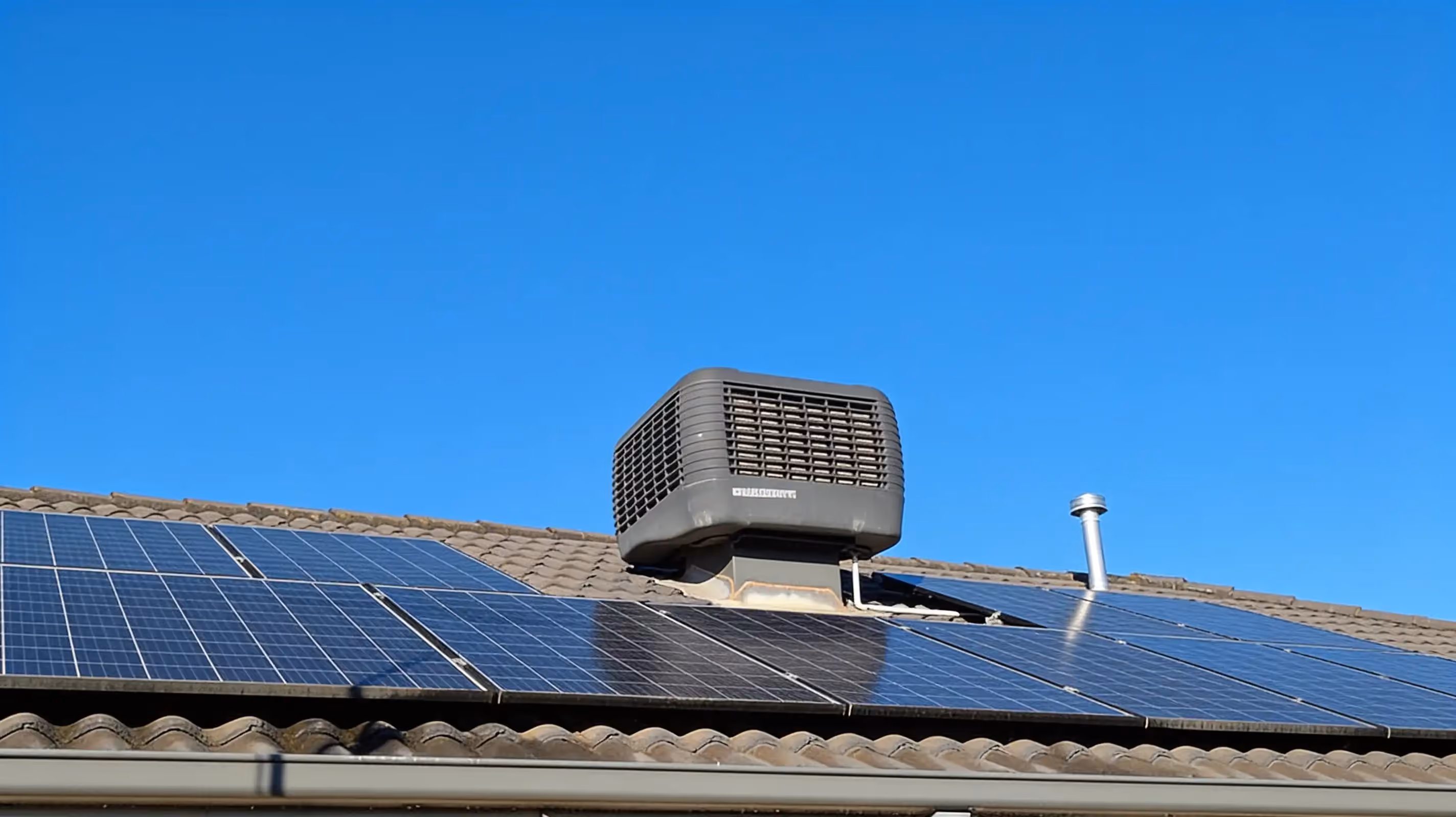 An evaporative cooler on a tiled roof beside rows of solar panels under a clear blue sky
